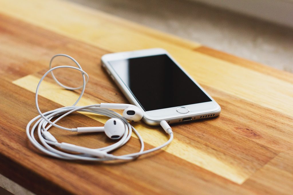 silver iPhone 6 with EarPods on brown wooden table