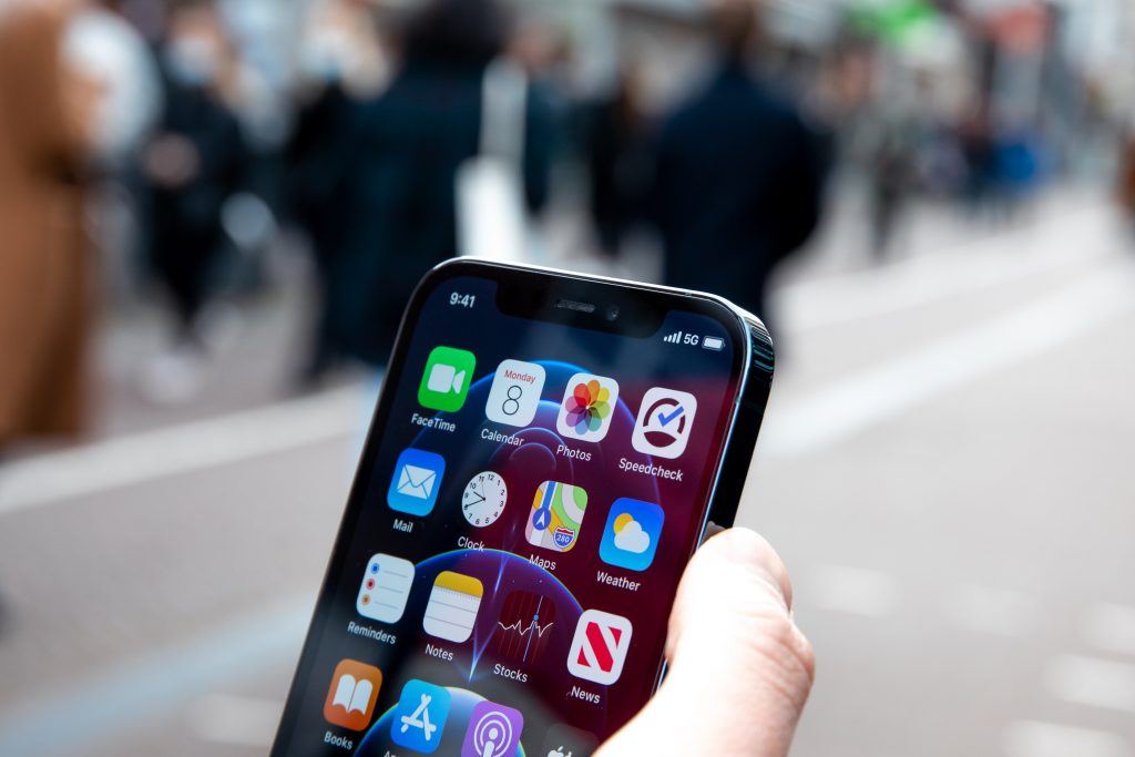 a person holding an iphone on road with blurry background of public