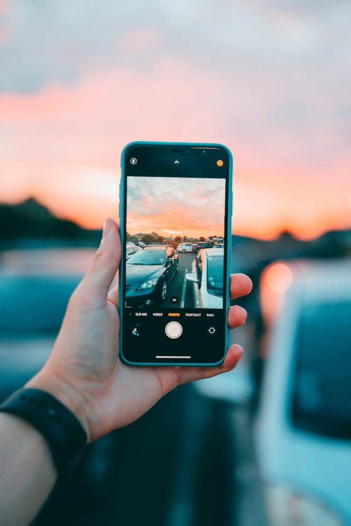 person holding an iphone and taking a picture of cars